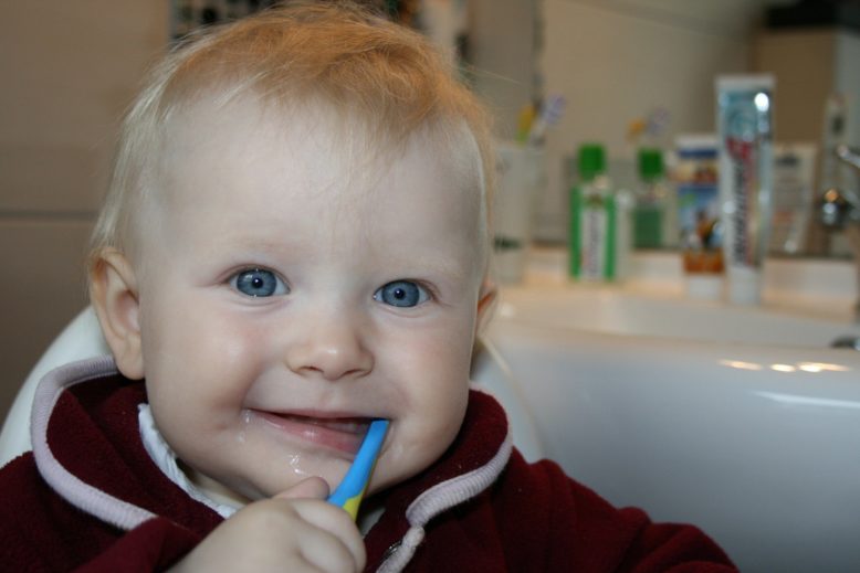 Rostro de bebé de ojos azules con cepillo en la boca como si estuviera cepillando los dientes. 