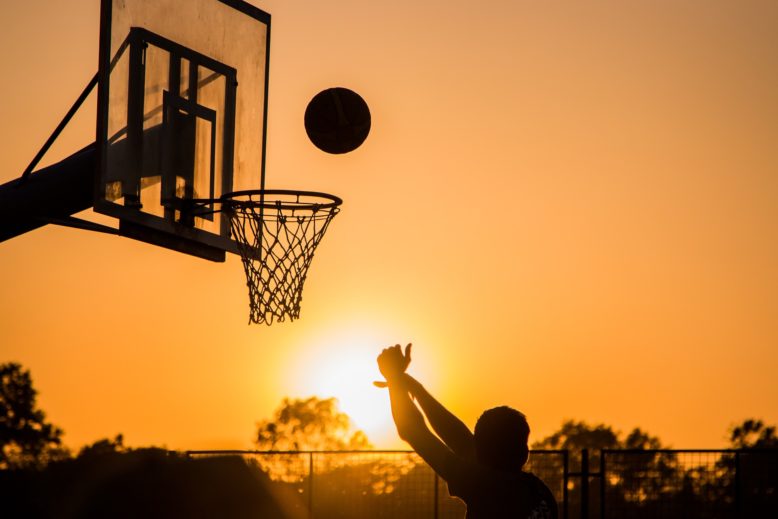 canasta de baloncesto, jugador que lanza la pelota en cancha al aire libre al atardecer
