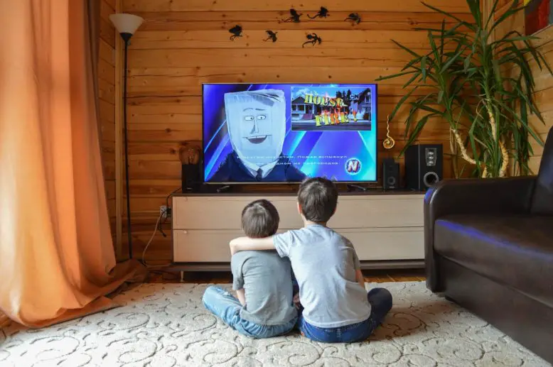 dos niños sentados en el piso de un living mirando televisión
